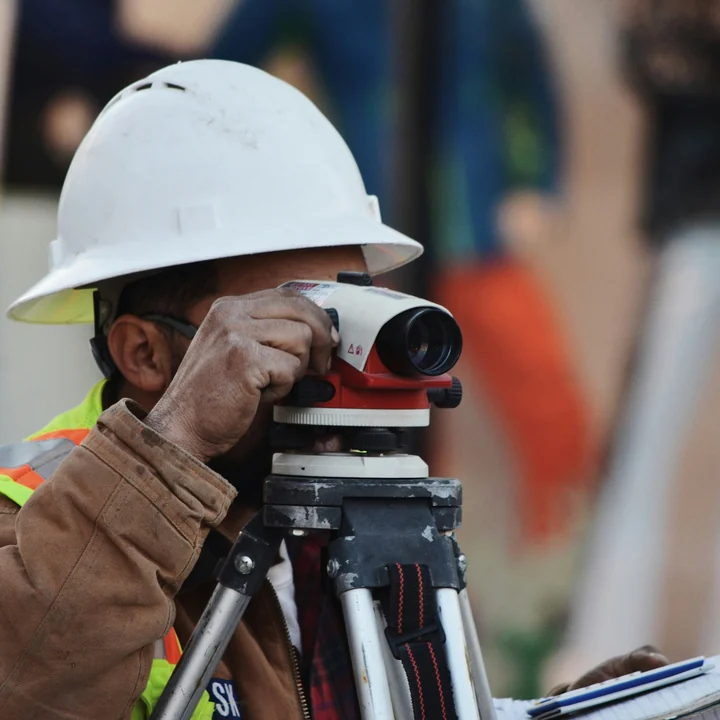 Un géomètre au casque blanc, l'œil au niveau de chantier