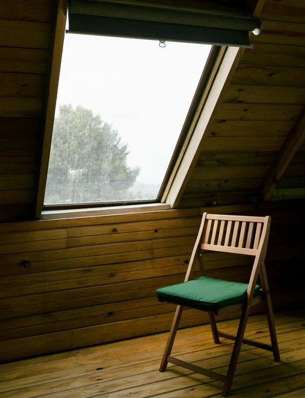Comble aménagé en bois, une chaise posée sous la fenêtre de toit